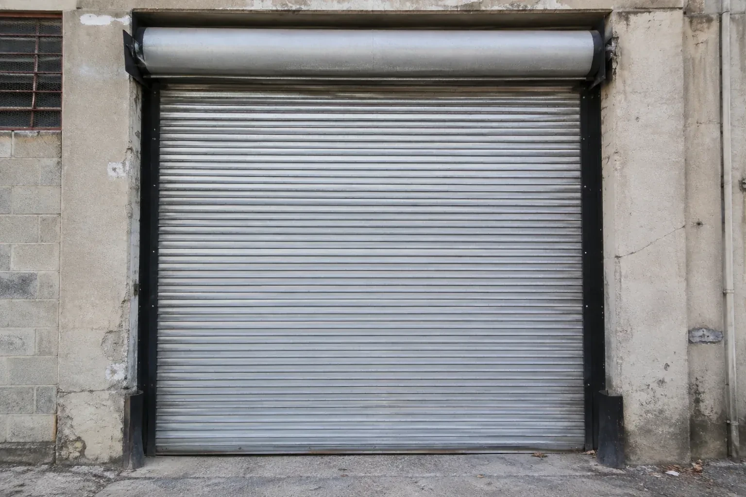 Closed metal rolling shutter in a weathered warehouse opening. — Commercial Rolling Door Repair, Whitchurch-Stouffville