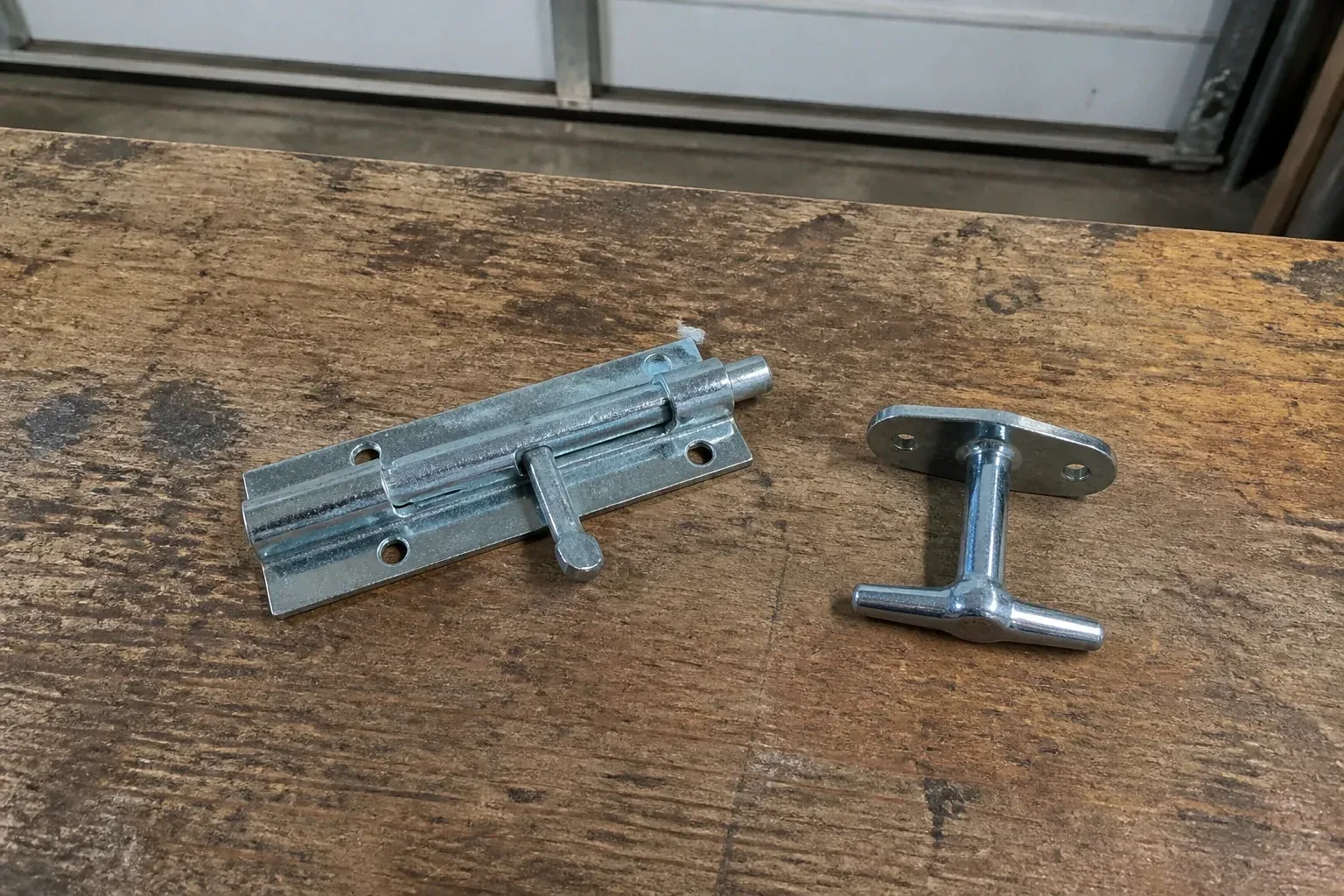 Detached slide bolt and T-handle on a wooden garage workbench. — Garage Door Manual Lock Repair, Whitchurch-Stouffville