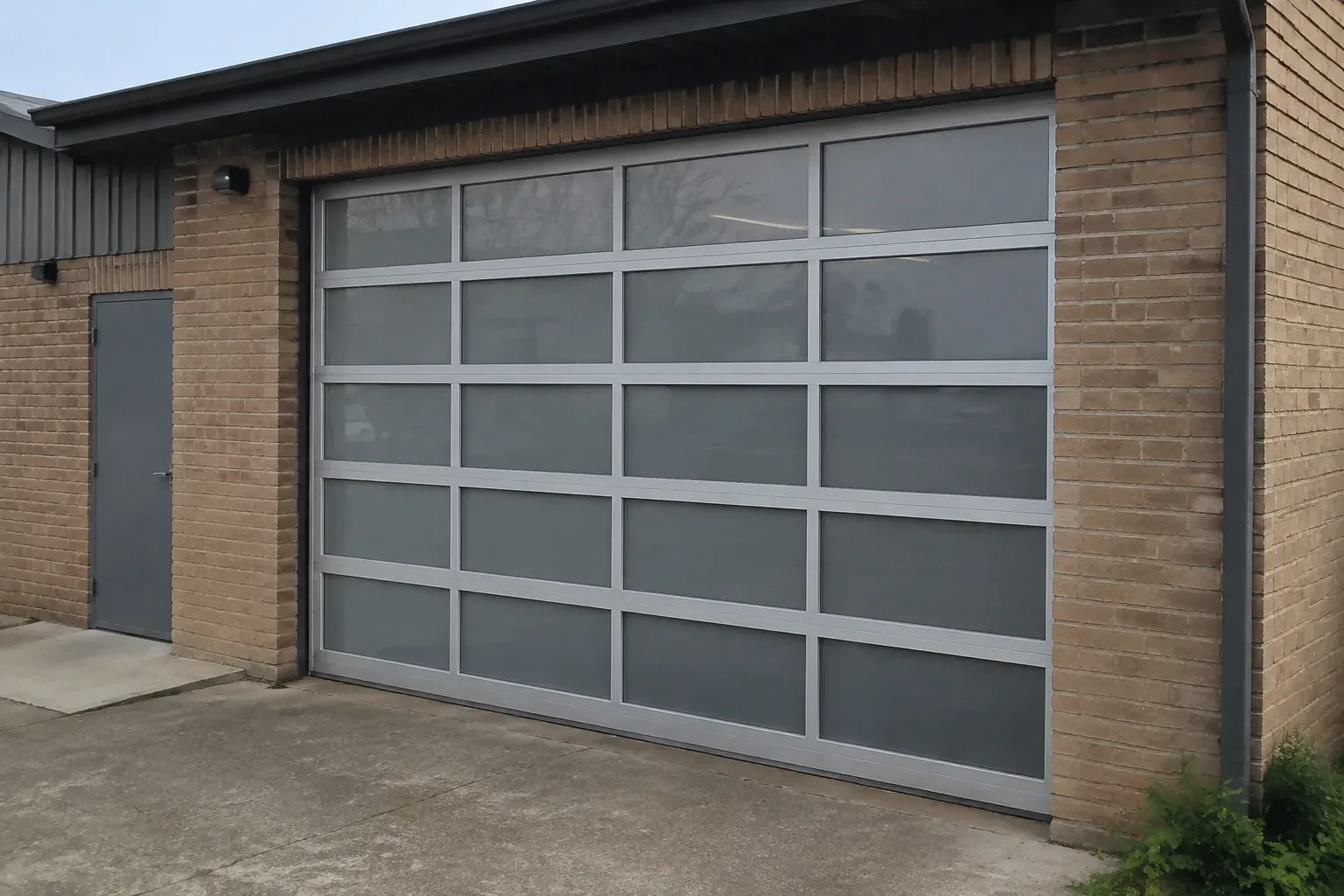 Closed glazed sectional door in a grey metal frame at a brick workshop. — Full-View Glass Garage Door Installation, Whitchurch-Stouffville